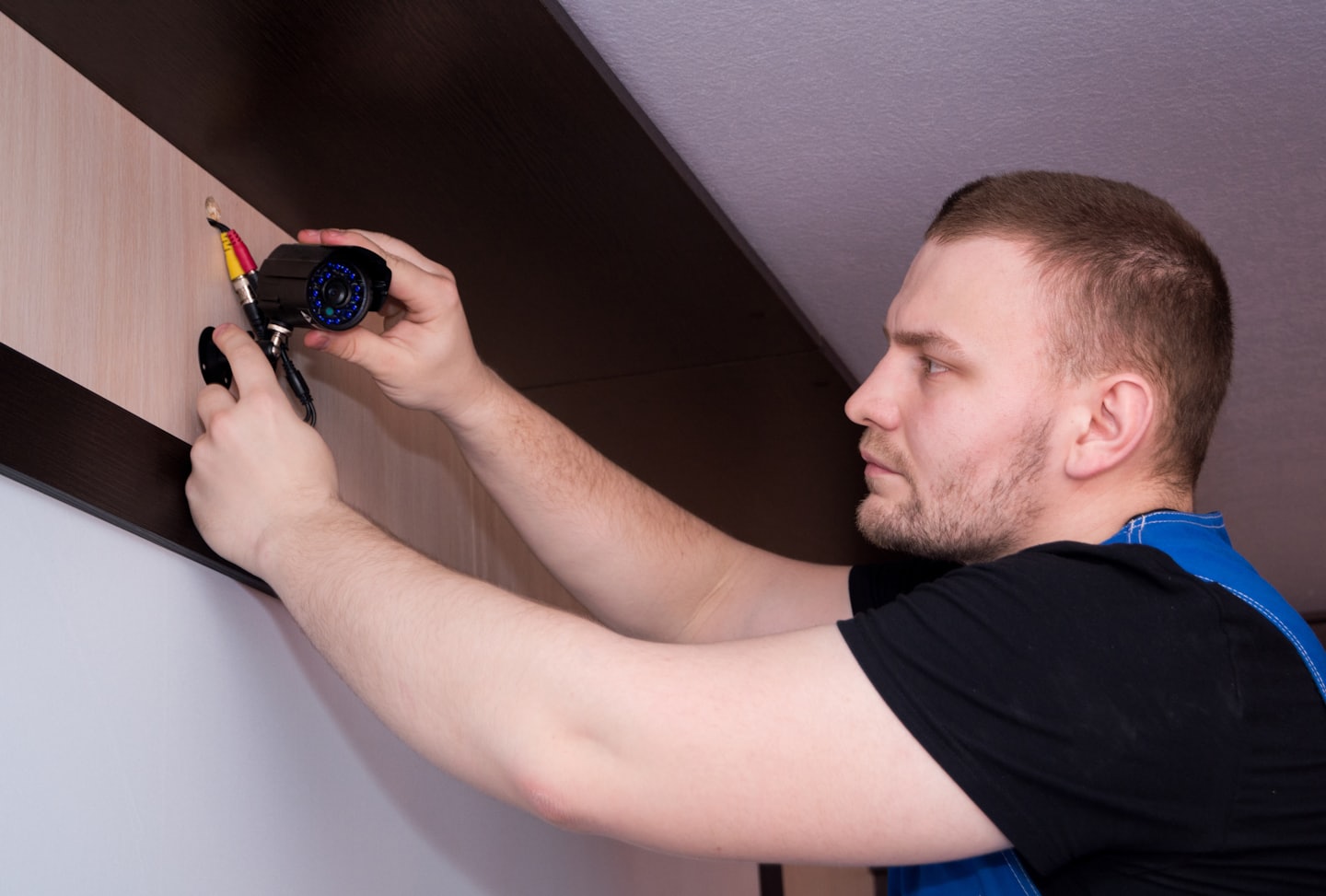 Technician installs a black security camera on a wood-paneled wall.